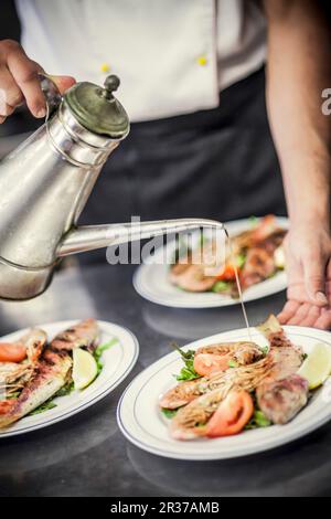 Hand fertig gegrillte Fische und Garnelen auf einem Teller mit Olivenöl Stockfoto