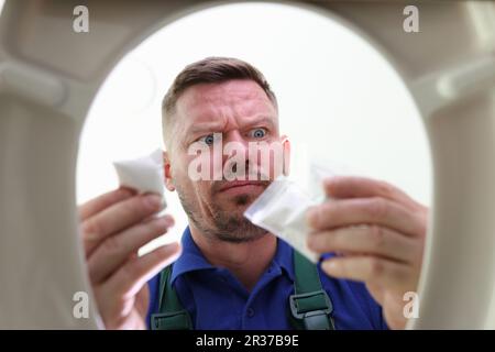 Ein unrasierter Mann steht über der Toilettenschüssel und hält Betäubungstüten Stockfoto