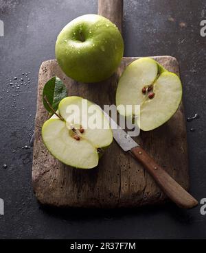 Granny Smith Äpfel, ganz und halbiert, auf einem alten Holzbrett mit einem Messer Stockfoto
