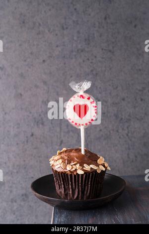 Ein Cupcake mit Schokoladeneis und Hafer mit einem herzförmigen Lolly oben Stockfoto