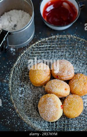 Donuts in einem Drahtkorb, eine Tasse Marmelade und eine Dose Puderzucker Stockfoto