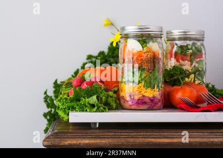 Zwei 2-in-1-Salate, die in Gläsern mit Spinat, Bohnen, Käse und Eier Stockfoto