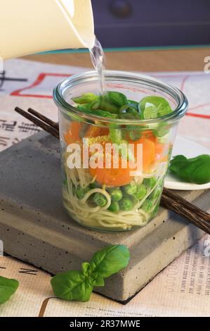 Asiatische Nudelsuppe in einem Glas zubereiten: Heißes Wasser zugeben und aufbrühen lassen Stockfoto