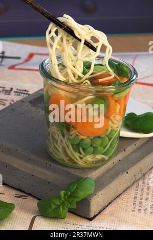 Asiatische Nudelsuppe mit Erbsen, Karotten und Basilikum in einem Glas Stockfoto