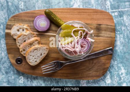 Eine Wurst, rote Zwiebel und Gurke Salat in einem Glas auf einem Holzbrett, mit Baguette Scheiben Stockfoto