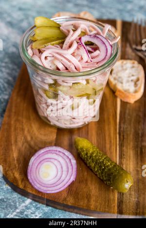 Wurst Salat mit roten Zwiebeln und Gewürzgurken in einem Glas auf einem Holzbrett Stockfoto