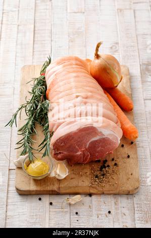 Rohes Schweinefleisch mit Zwiebeln, Karotten, Rosmarin und Gewürzen auf einem Schneidebrett Stockfoto