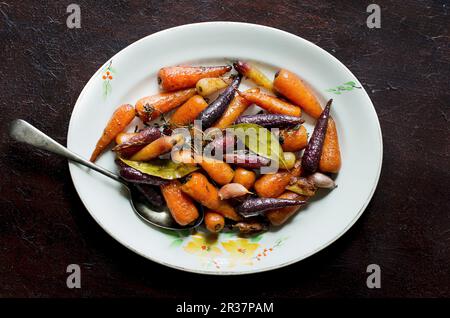 Glasierte bunte Karotten, Knoblauch, Lorbeer und Thymian (Ansicht von oben) Stockfoto