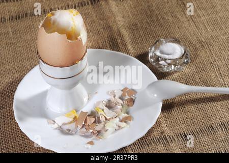 Weich gekochtes Ei in einem Keramikeibecher mit flüssigem gelbem Eigelb und passendem weißem Keramiklöffel Stockfoto