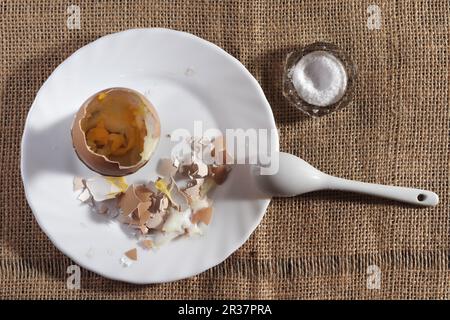 Weich gekochtes Ei in einem Keramikeibecher mit flüssigem gelbem Eigelb und passendem weißem Keramiklöffel Stockfoto