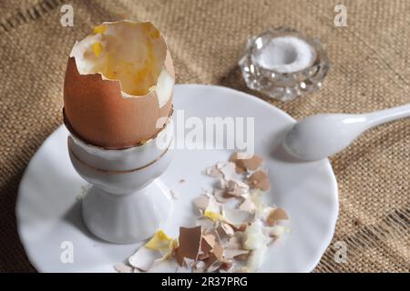 Weich gekochtes Ei in einem Keramikeibecher mit flüssigem gelbem Eigelb und passendem weißem Keramiklöffel Stockfoto