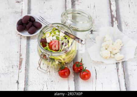 Zoodles (Zucchini-Nudeln) in einem Glasgefäß mit Tomaten, Feta und Oliven Stockfoto