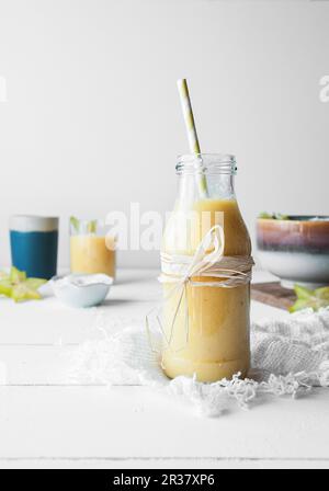 Mango- und Ananas-Smoothie, serviert in einer Glasflasche mit einem Strohhalm Stockfoto