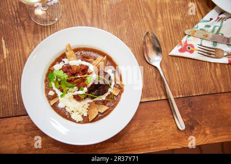 Cremige Bohnensuppe mit gebratenen Tortilla-Streifen, Chorizo, Chilisringen, Sauerrahm, Feta und Koriander (Mexiko) Stockfoto