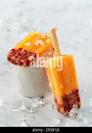 Mango- und Granatapfeleis Lollies auf Stöcken mit zerstoßenem Eis Stockfoto