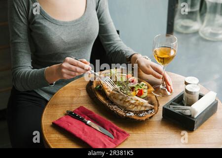 Eine Frau isst gegrillte Makrele und Gemüse auf einem Holzbrett Stockfoto