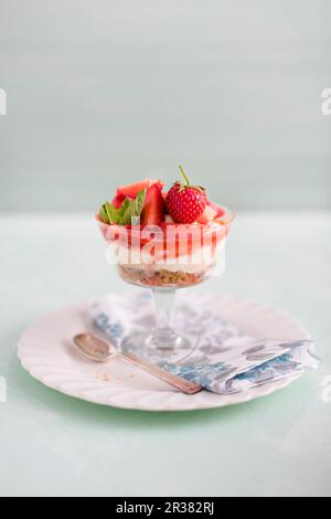 Erdbeer- und Vanillekäsekuchen mit Nuss- und Keksbasis in einem Glas Stockfoto