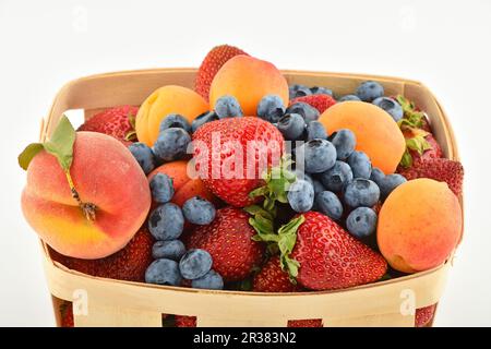 Erdbeeren, Aprikosen, Heidelbeeren, Pfirsiche im Korb, isoliert auf weiß Stockfoto