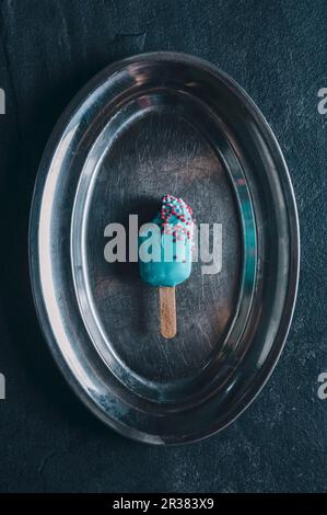 Ein Kuchen-Pop in Form eines Eislollys mit bunten Glasuren auf einem silbernen Tablett Stockfoto