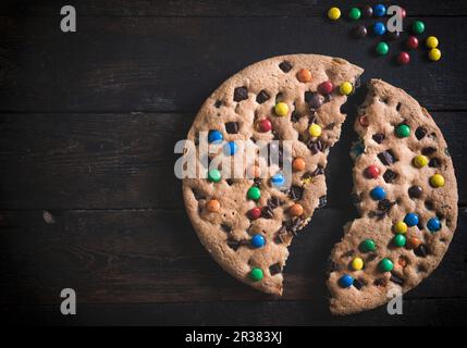 Ein riesiger Schokokeks mit bunten, zuckerbeschichteten Schokoladenkeksen, zerbrochen Stockfoto