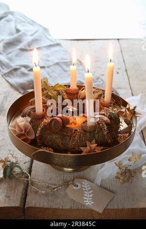 Ein traditioneller Adventskranz auf einem goldenen Stand mit einem handbemalten Etikett auf einem rustikalen Tisch Stockfoto