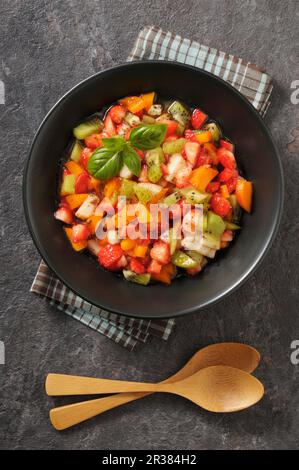 Obstsalat mit Erdbeeren, Aprikosen, Pfirsichen, Kiwis und Basilikum Stockfoto