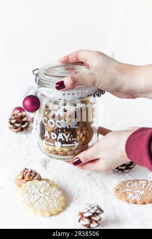 Hände mit einem Glasglas mit dekorierten Weihnachtskeksen Stockfoto