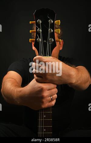 Mann mit Gitarre Hals mit beiden Händen isoliert auf Schwarz Stockfoto