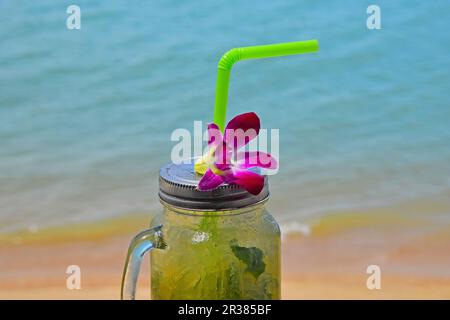 Großes Glas Mojito mit orchideenblüte am Strand Stockfoto