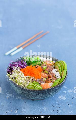 Eine Poke-Schüssel mit Wakame-Algen, Thunfisch, Sushi-Reis, Lachs, Luzerne, Rotkohl, Sesamsamen, Gurkenscheiben, Frühlingszwiebeln, Avocado, Und an Stockfoto