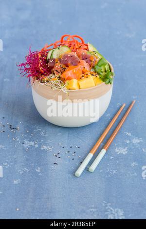 Eine Poke-Schüssel mit Thunfisch, Lachs, Sushi-Reis, Tobiko, Avocado, Karotten, Mango und Sprossen Stockfoto