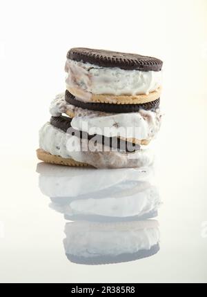 Ein Stapel Eiscremesandwiches schmilzt und spiegelt sich auf einer glänzend weißen Oberfläche wider Stockfoto