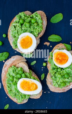 Toast mit pürierten grünen Erbsen, gekochtem Ei und frischem Basilikum Stockfoto