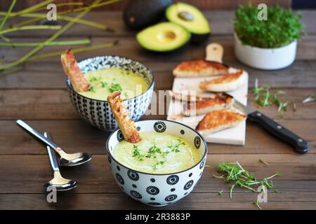 Avocado-Suppe in zwei Schüsseln auf einem rustikalen Tisch mit Toast und frischer Kresse Stockfoto