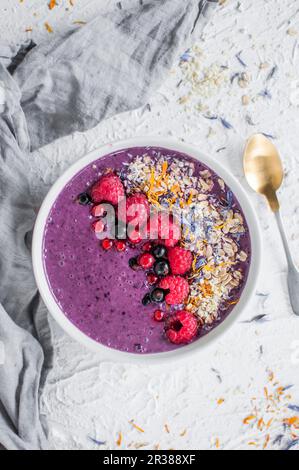 Eine Schüssel mit Heidelbeeren-Smoothie mit Beeren, Blüten, Chia und Hirse Stockfoto