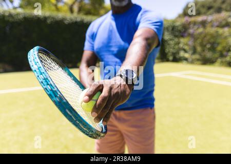 Mittelteil eines erfahrenen afroamerikanischen Mannes, der Tennis spielt und sich auf einen sonnigen Rasenplatz vorbereitet Stockfoto