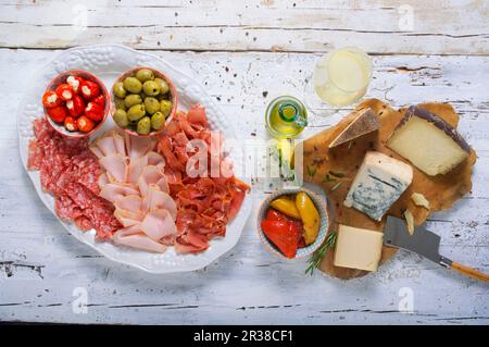 Käse- und Wurstplatte mit Oliven, gefülltem Gemüse und Weißwein Stockfoto