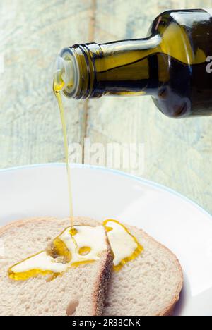 Händen gießt Olivenöl auf Brot Stockfoto
