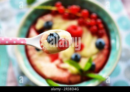 Vanille mit frischem Obst und Obstsirup auf einem Löffel über einer Schüssel Stockfoto