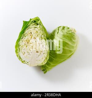 Spitz zulaufende Kohlköpfe, ganz und halbiert, auf einer weißen Oberfläche Stockfoto