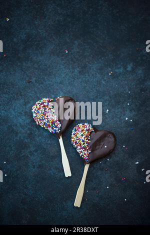 Heart-shaped vegane Kekse auf Sticks mit Zartbitter-schokolade und Streuseln Stockfoto