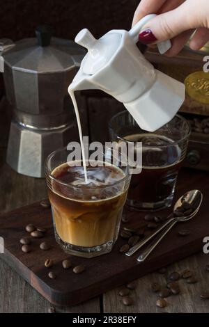 Milch wird in ein Glas Kaffee gegossen Stockfoto