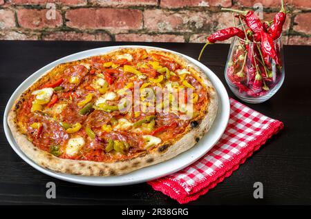 Pizza mit Sauerteig Base, Tomatensauce mit Oregano und Olivenöl, Mozzarella, grüne, gelbe und rote Paprika, würzige Salami, Peperoni, Stockfoto