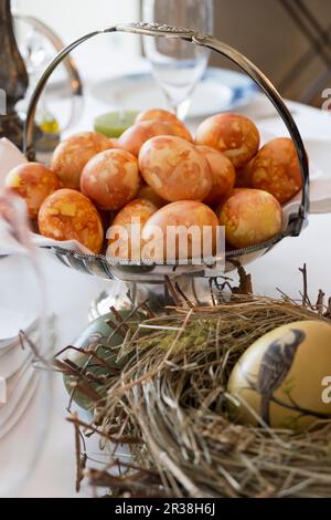 Braune Eier in einer Silberschale hinter einem bemalten Osterei in einem Strohnest Stockfoto