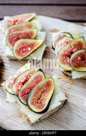 Bruschetta geröstetes Sauerteigbrot mit Käse und Feigen, mit Honig bespritzt auf einem weißen hölzernen Servierbrett auf einem Holztisch Stockfoto