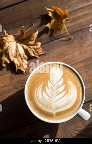 Flache weiße, Cappuccino mit Rosetta oder florette Latte Art auf einer hölzernen Hintergrund mit Blätter im Herbst Stockfoto