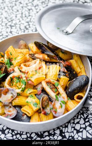 Mezze Maniche rigatoni Pasta mit Meeresfrüchten, Calamari, Tintenfisch, Muscheln, Muscheln, Cockles, Petersilie, Tomatensoße Stockfoto