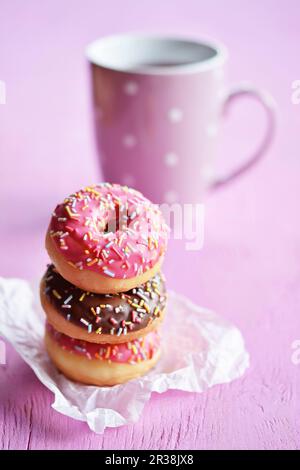 Ein Stapel drei Mini-Donuts mit Puderzucker und Zuckersträngen vor einer Teetasse Stockfoto