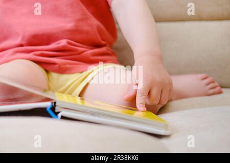 Das niedliche Baby spielt mit dem bunten Bilderbuch, blättert durch die Seiten und berührt die Bilder. Das kleine Kind ist in Gedanken verloren als Stockfoto