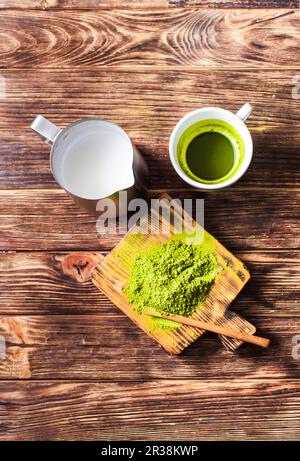 Matcha Tee mit Pulverisiertem grüner Tee und Milchkännchen auf einem dunklen Holzmöbeln im Landhausstil. Stockfoto